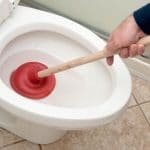 Clean white toilet with red plunger in bowl, showcasing plumbing maintenance and DIY tips from Scott Plumbing.