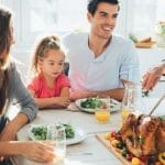 Two adults and a child enjoying a meal at a dining table with salads and roasted chicken, representing family togetherness.