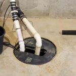 Installation of sump pump with PVC pipes and basin in a basement by Scott Plumbing, featuring concrete flooring and wiring.