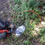 Garden tool with orange cord in grassy area for yard maintenance and plumbing-related landscaping tasks.