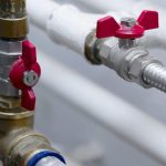 Close-up of metal valves with red handles on industrial piping for plumbing solutions by Scott Plumbing.