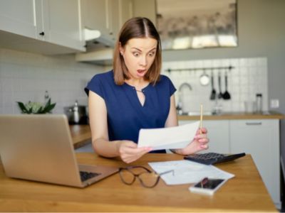 Woman surprised by high water bill while reviewing documents at kitchen table, illustrating the impact of plumbing leaks on household expenses.